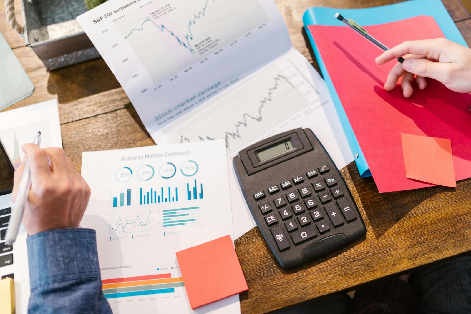 Hands analyzing financial data, charts, and metrics with a calculator and folders, symbolizing strategies to improve your money mindset.